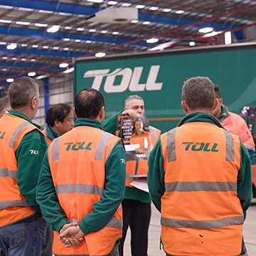 Toll employees in uniform in a team meeting, presenting the posters Chello has designed