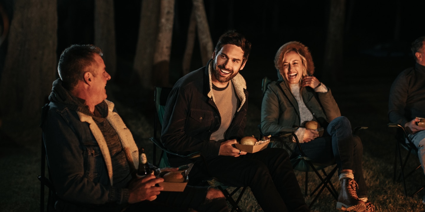 Lead couple for the Ingenia Holidays shoot laughing at a joke around the campfire.